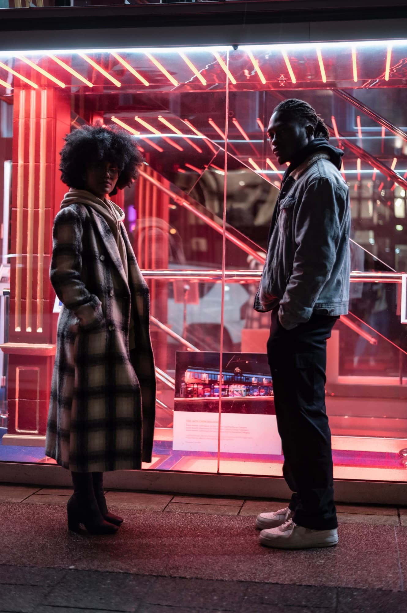 A stylish couple by a glass building at night
