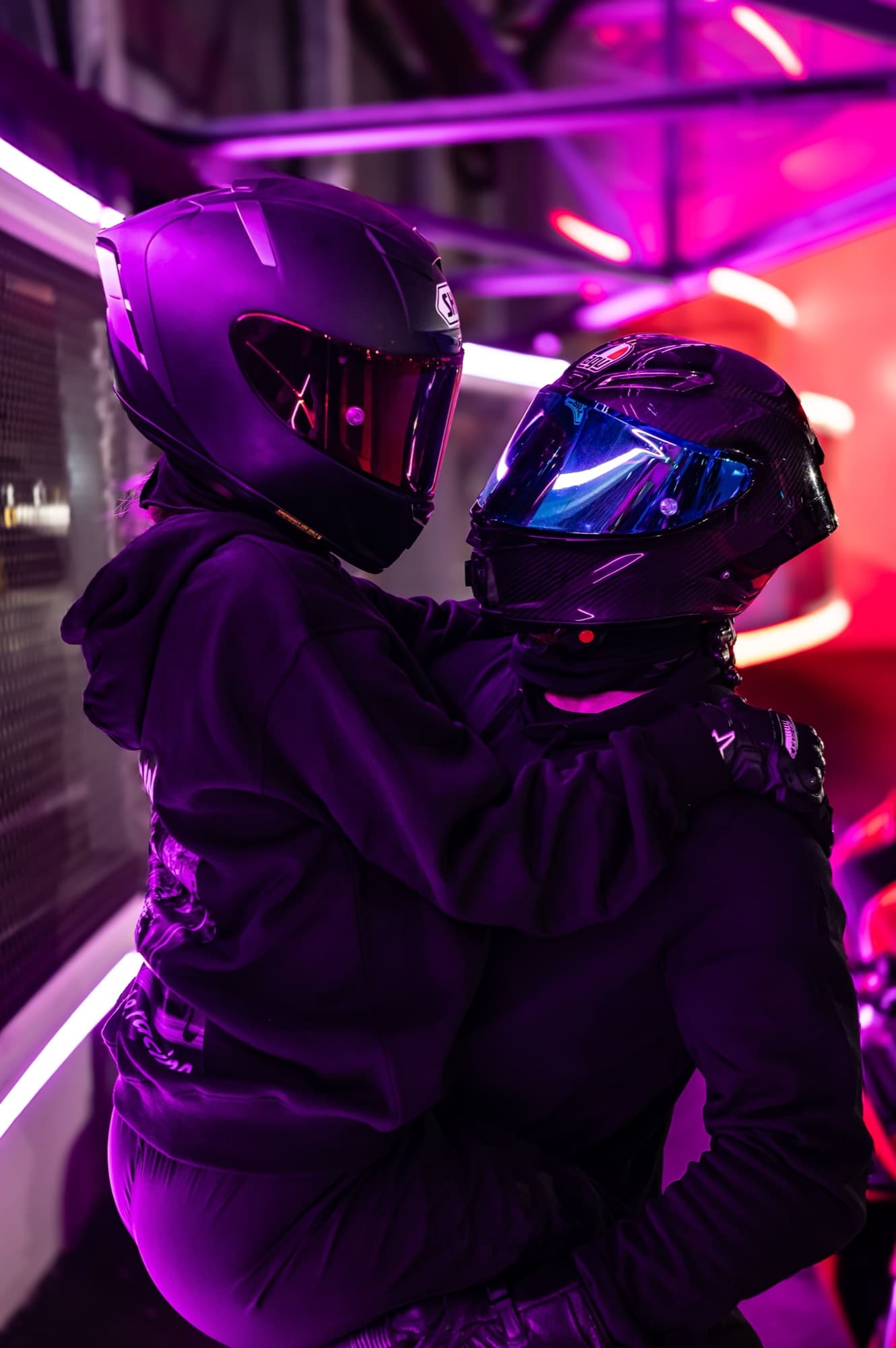 A couple embracing in motorcycle helmets under purple and red light