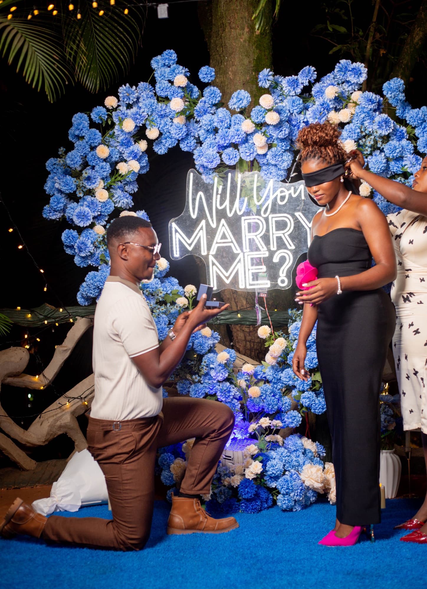A marriage proposal in front of a neon sign reading Will You Marry Me